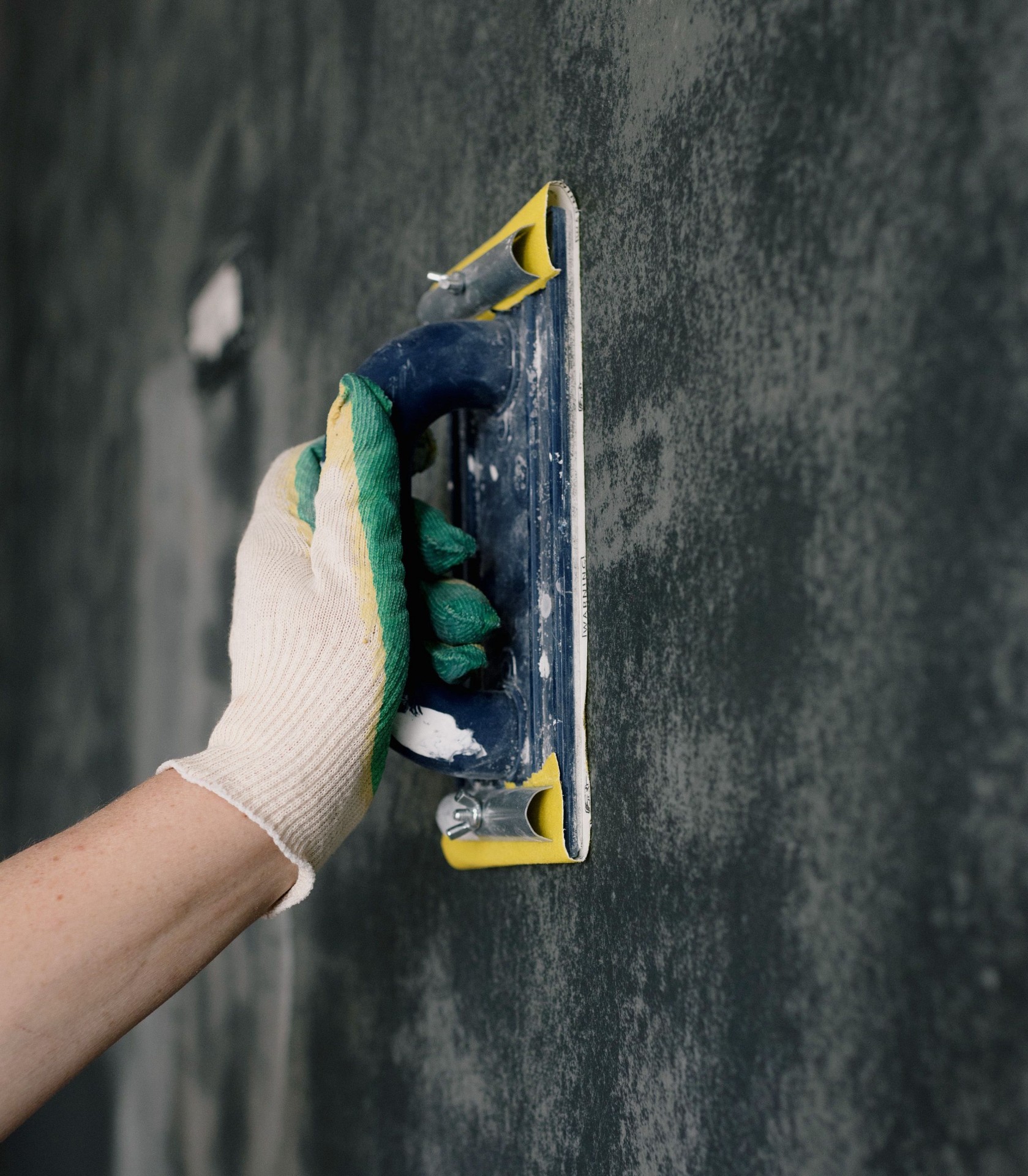 Gloved hand sanding and preparing a wall surface before painting